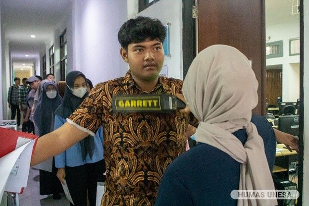 Pengawas mengecek dan memastikan peserta bersih dari bawaan yang dilarang saat tes UTBK menggunakan metal detector.